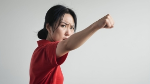 拳を前に突き出す赤いポロシャツを着た黒髪の女性 / 拳で抵抗する女性のフリー素材・写真・画像